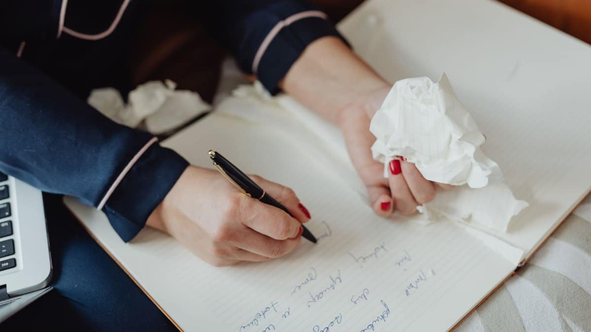 Hands writing in a notebook with crumpled paper, focus on creativity and ideas.