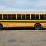 Empty yellow large school bus parked on asphalt road under cloudy blue sky in daytime