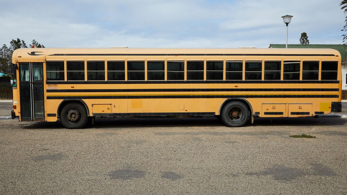 Empty yellow large school bus parked on asphalt road under cloudy blue sky in daytime