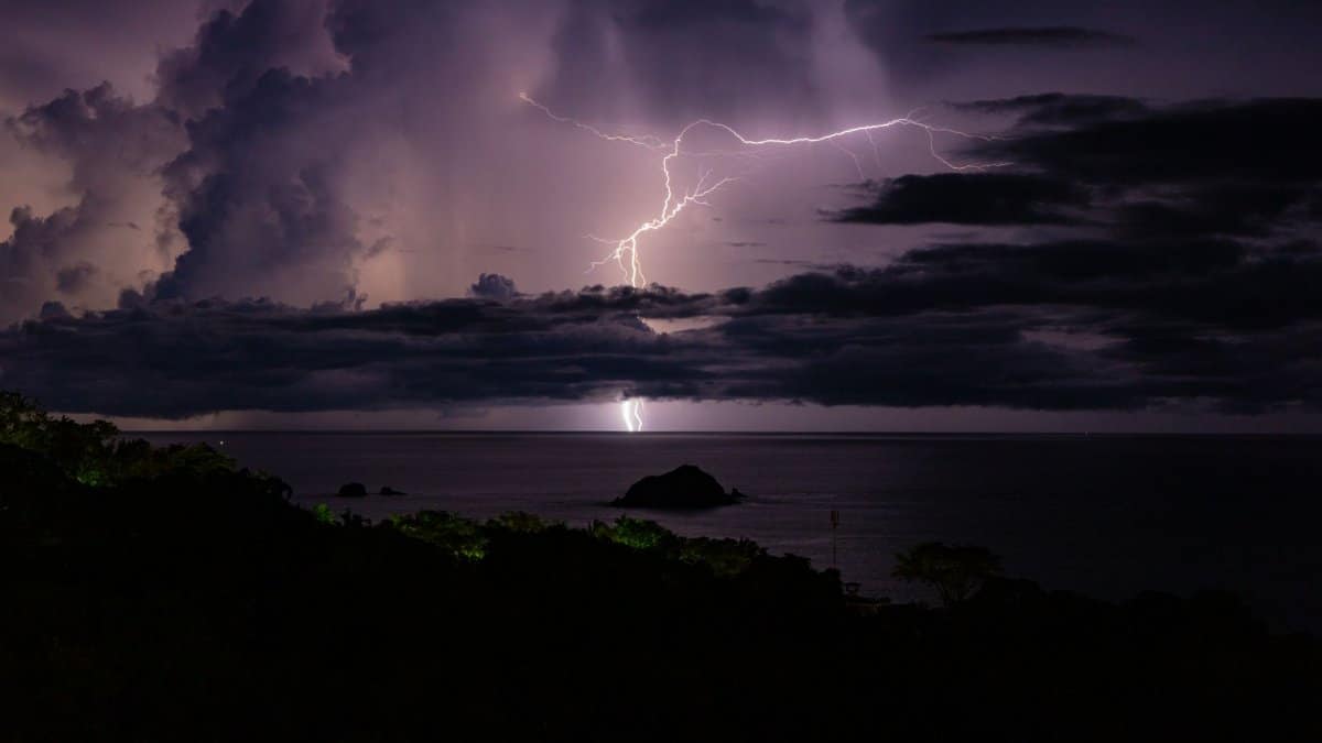 Powerful lightning illuminates a dark ocean scene under dramatic storm clouds.