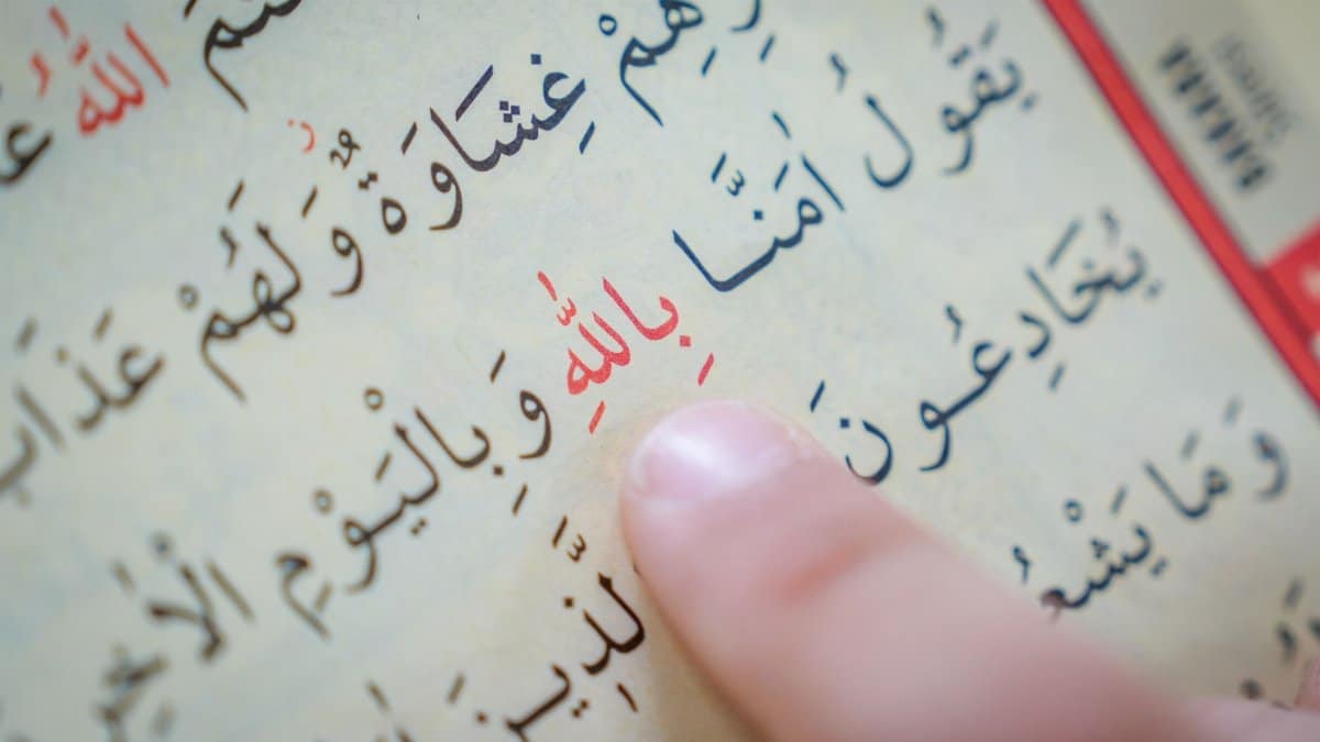 Close-up of a finger pointing at Arabic text in a religious book, emphasizing study or learning.