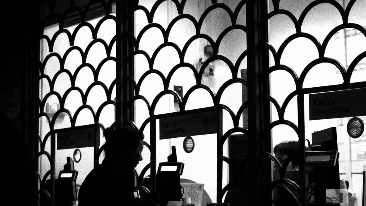 Silhouetted woman at a ticket office window, captured in black and white for a dramatic effect.