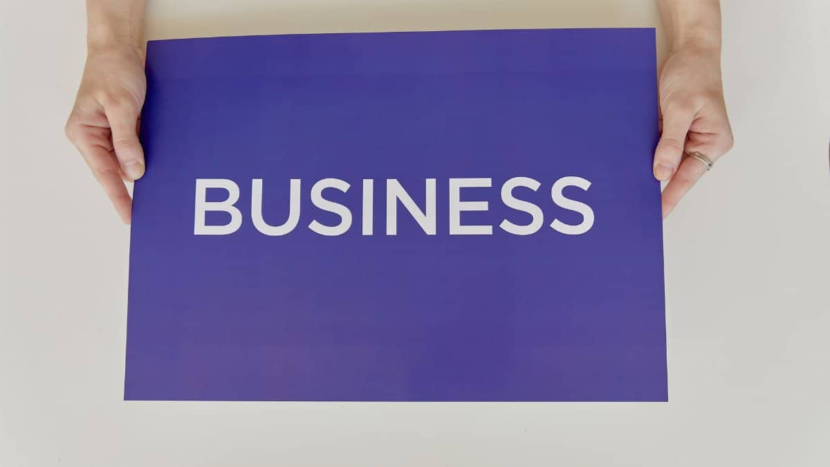 Hands holding a purple sign with the word 'BUSINESS', symbolizing corporate concepts.