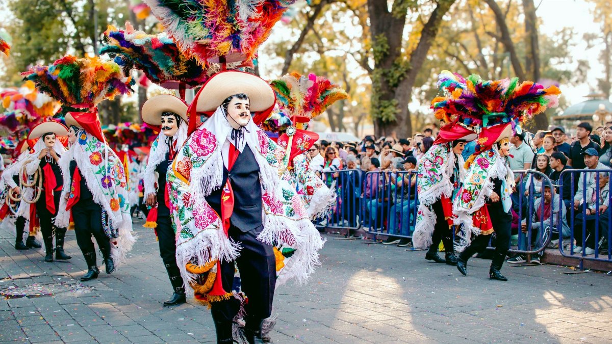 Colorful festival parade featuring traditional costumes and feathered hats, attracting a lively crowd.
