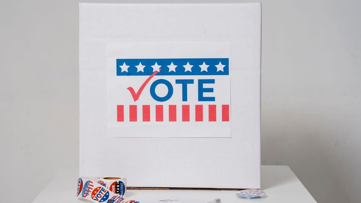 Ballot box with vote sign surrounded by voting stickers, indicating election theme.