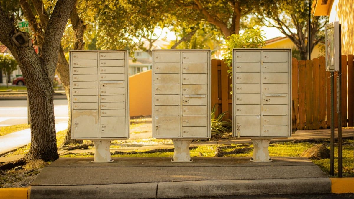 Three cluster mailboxes under trees in a residential area of Florida, USA, on a sunny day.