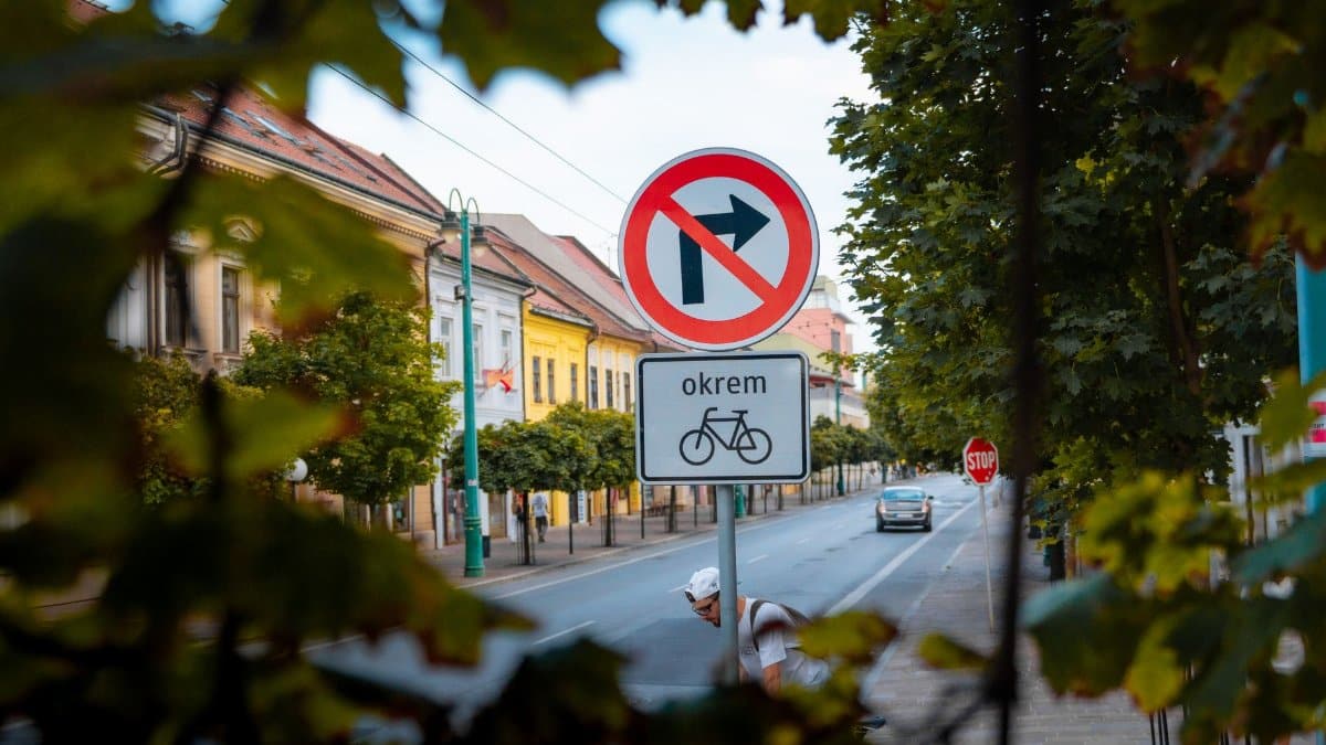 Urban street view featuring a no right turn sign and cyclist in a leafy European city.