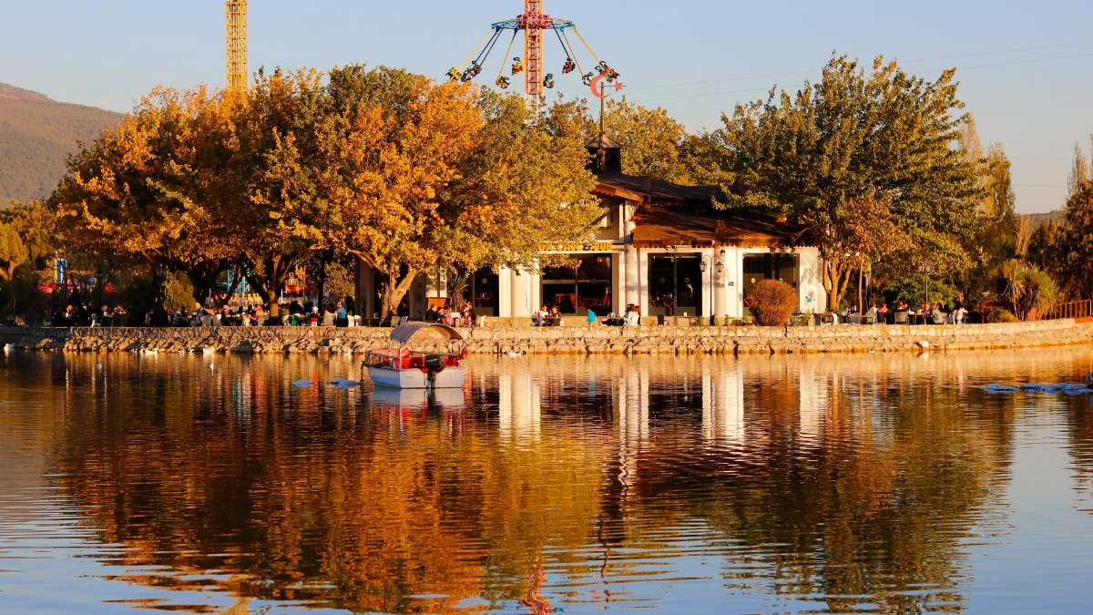 Charming autumn scene featuring an amusement park by a tranquil lake at sunset. Reflections and golden hues create a peaceful atmosphere.