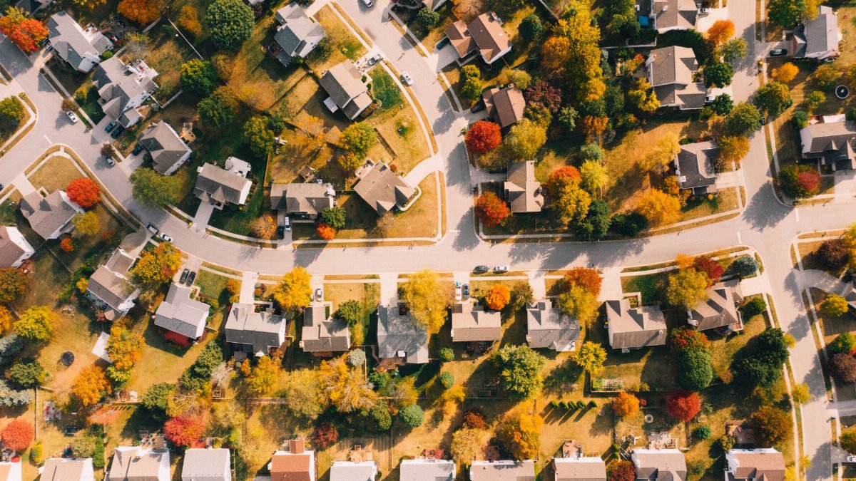Aerial view of residential building roofs between lawns with colorful trees and roadways in fall