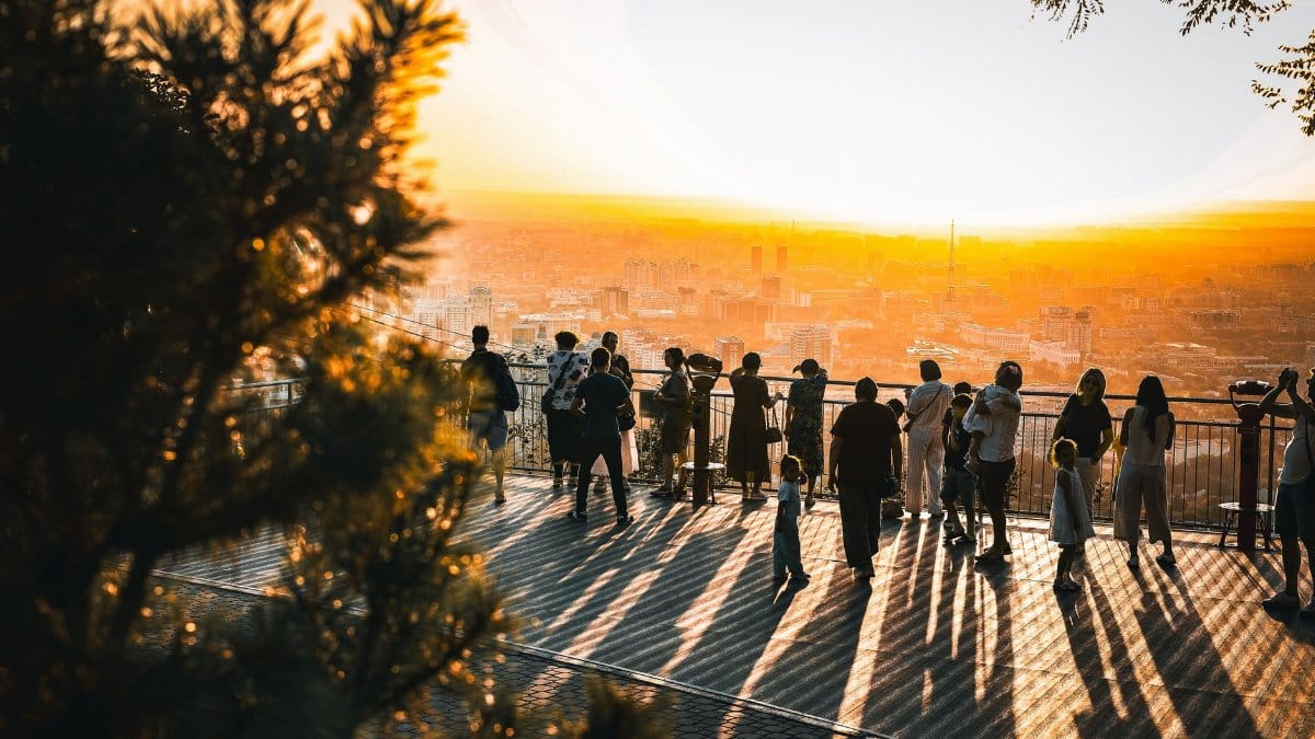 People enjoying a stunning sunset view over Almaty from Kok-Tobe, casting long shadows.