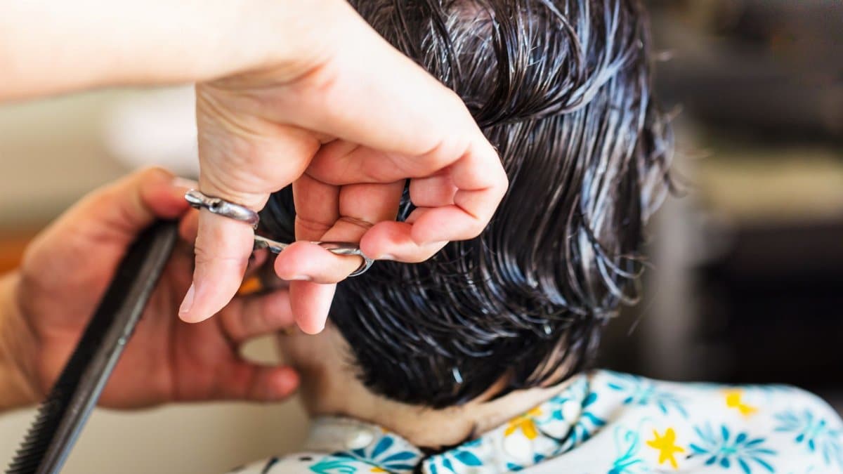 Close-up of a hairstylist cutting short wet dark hair at a salon.