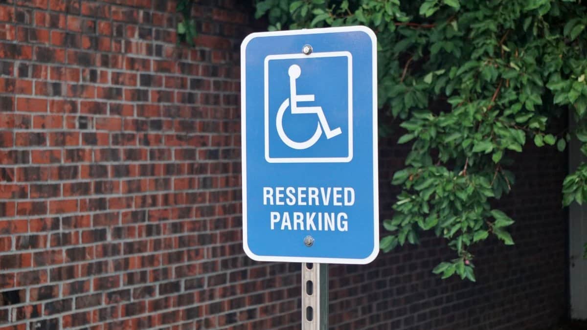 Blue sign indicating reserved parking space for disabled access by a brick wall.