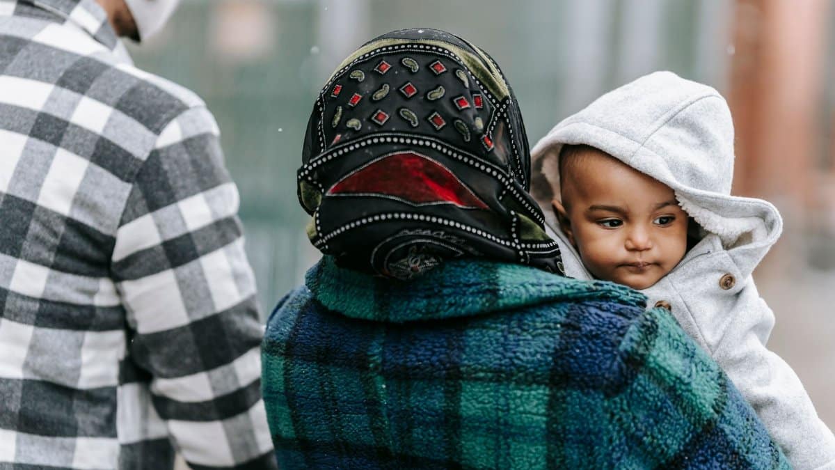 Anonymous father and mother with African American baby in warm outerwear on hands walking on street in city on blurred background