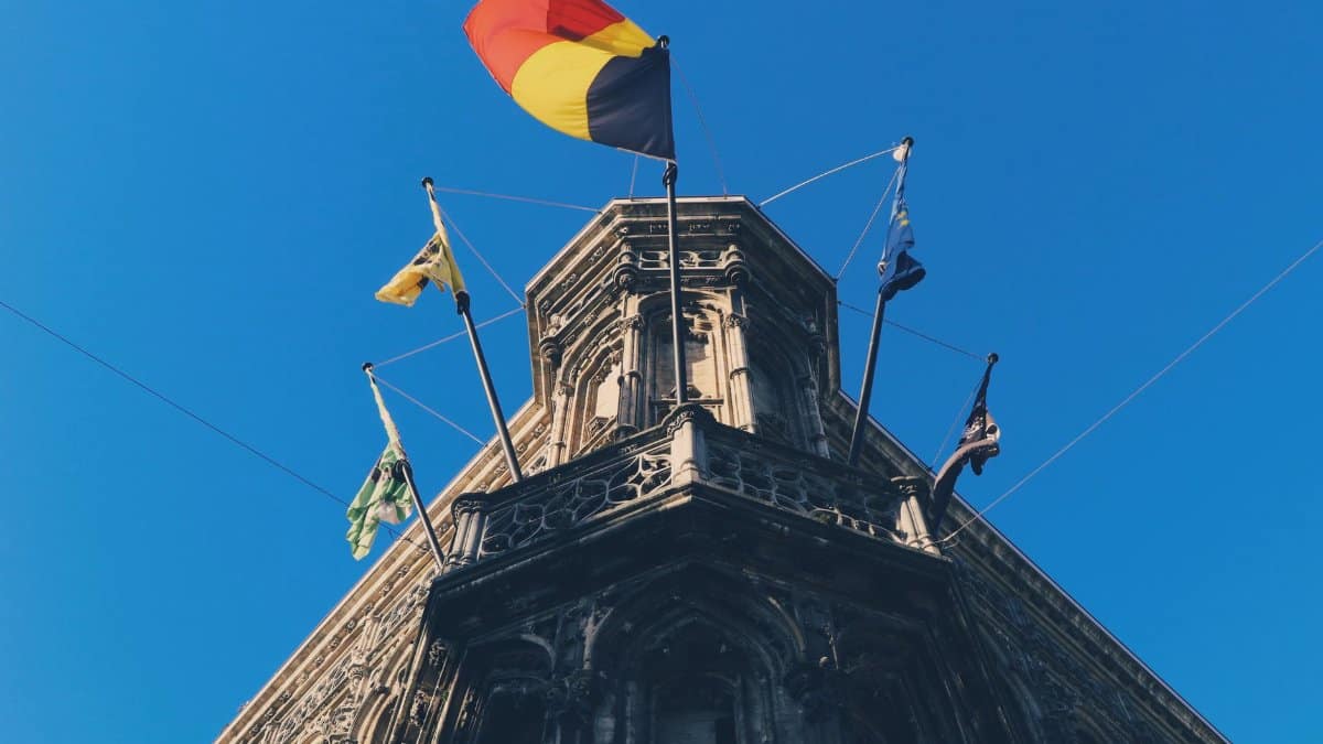 Historic building in Ghent with Belgian and regional flags against a clear blue sky.
