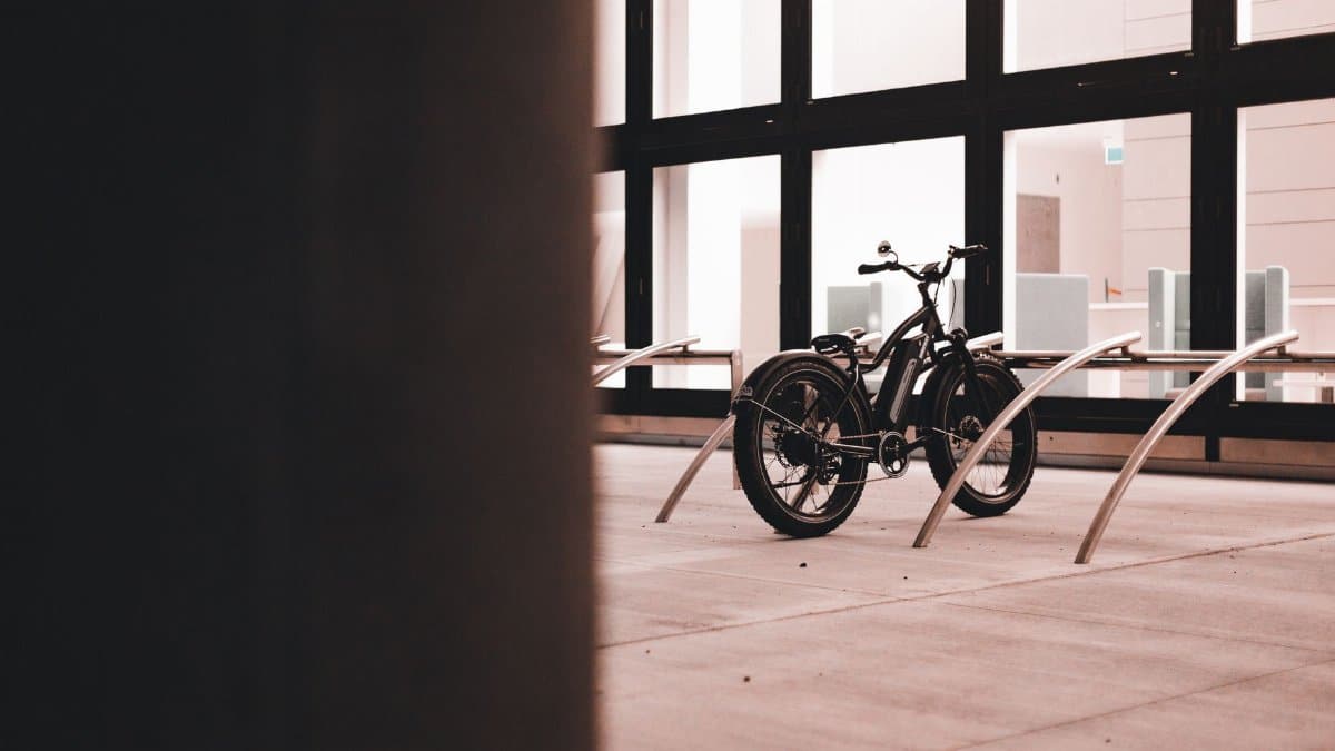 A modern electric bicycle parked indoors near a large glass wall with steel racks.