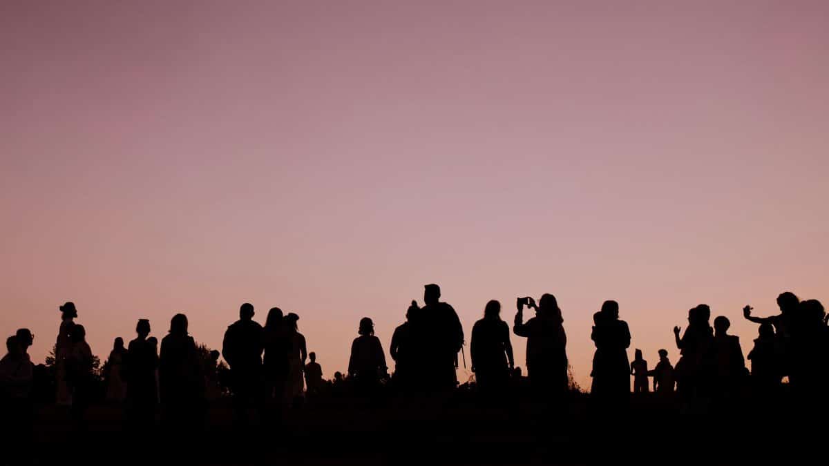 Silhouettes of people gathered outdoors during a stunning sunset, creating a captivating scene.