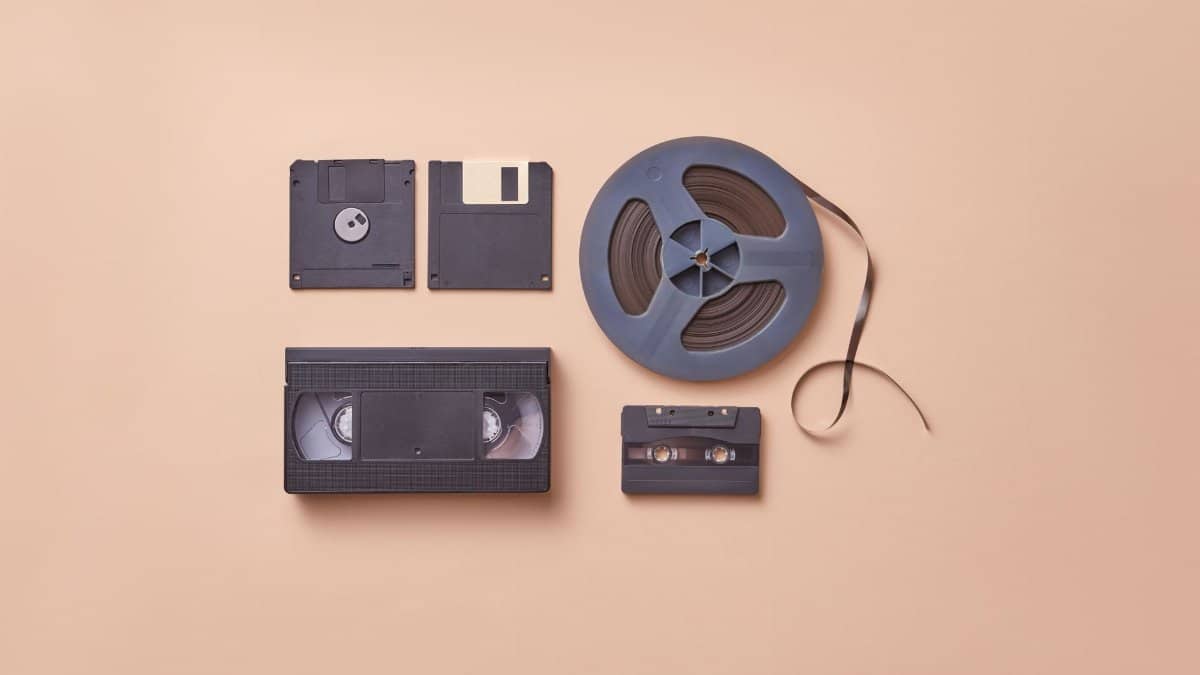 A collection of vintage media storage formats including VHS, cassette, and floppy disks on a beige background.