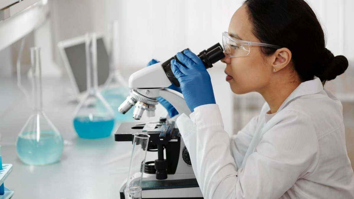 Female scientist in a laboratory examining samples through a microscope for research.
