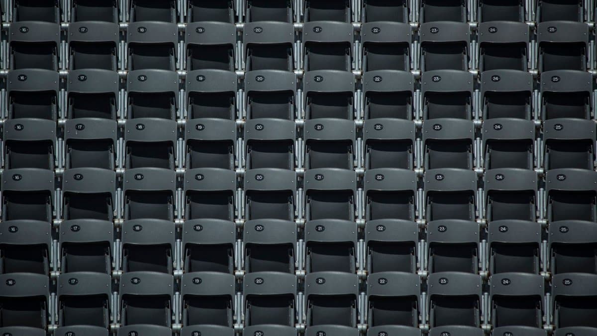 Symmetrical rows of empty gray seats in an indoor stadium or auditorium setting, perfect for abstract design concepts.