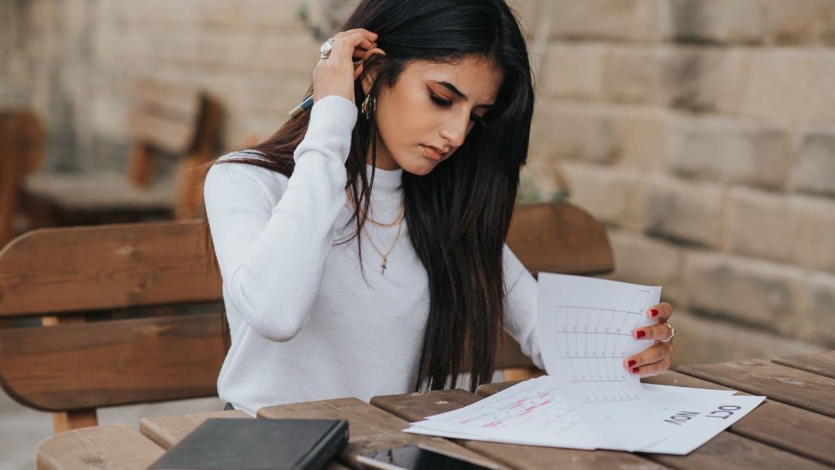 Young ethnic female student in casual outfit with dark hair at wooden table looking through plans in calendar