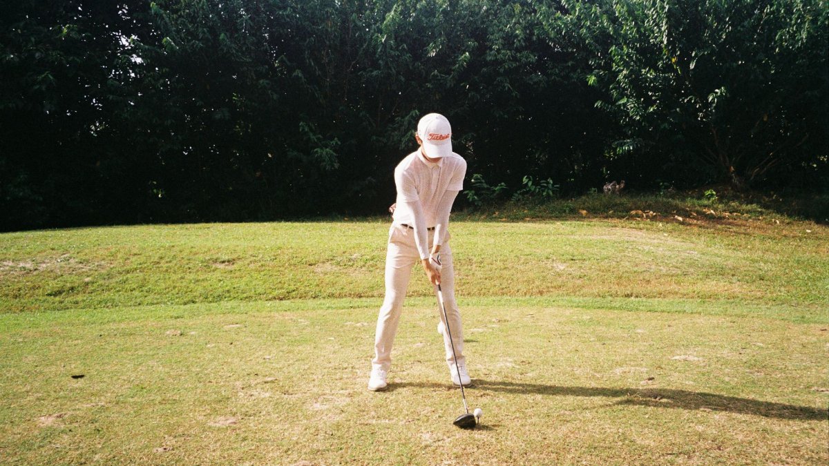 A golfer in white attire getting ready to tee off on a sunny day at a golf course.
