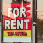 Reflection of a cityscape on a window with a 'For Rent' sign and sunset glow.