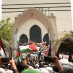 A large pro-Palestinian protest in Dhaka, Bangladesh with flags and banners.