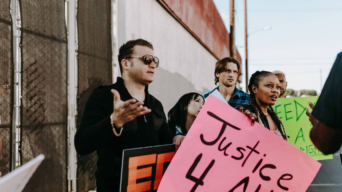 A diverse group of people holding signs advocating for justice and human rights in an outdoor protest.