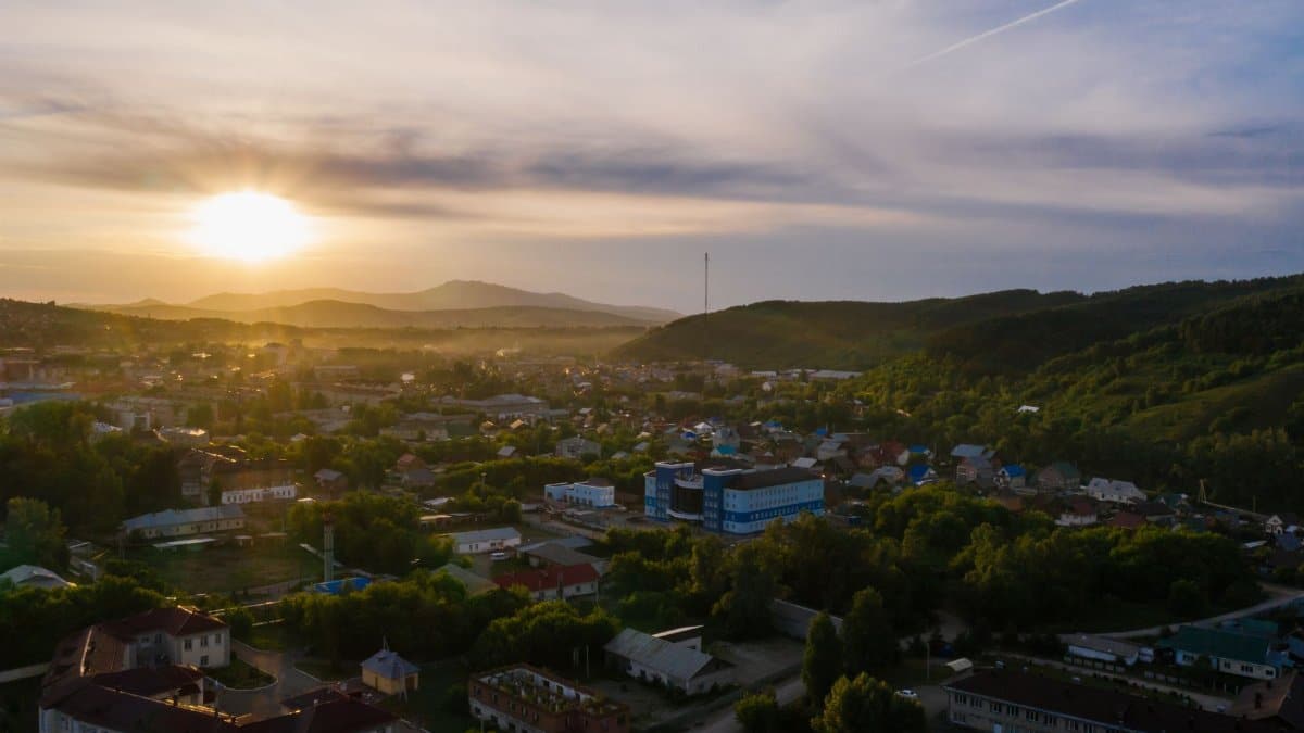 A breathtaking aerial view of an urban area with lush greenery and mountains at sunrise.