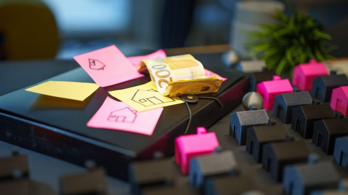 Euro banknotes on laptop with sticky notes and house models, symbolizing real estate investment.