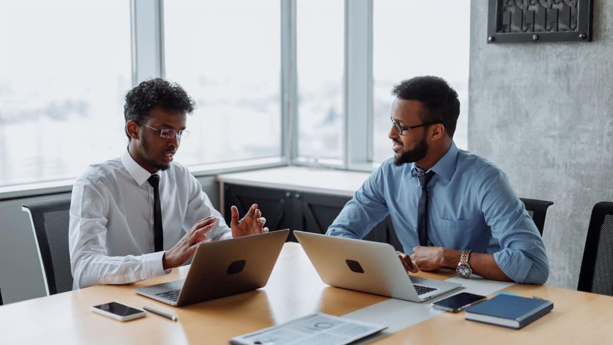 Two African American professionals discussing a project in an office with laptops.