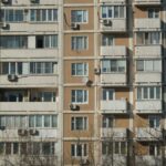 Front view of a sunlit urban apartment building with balconies and air conditioning units.