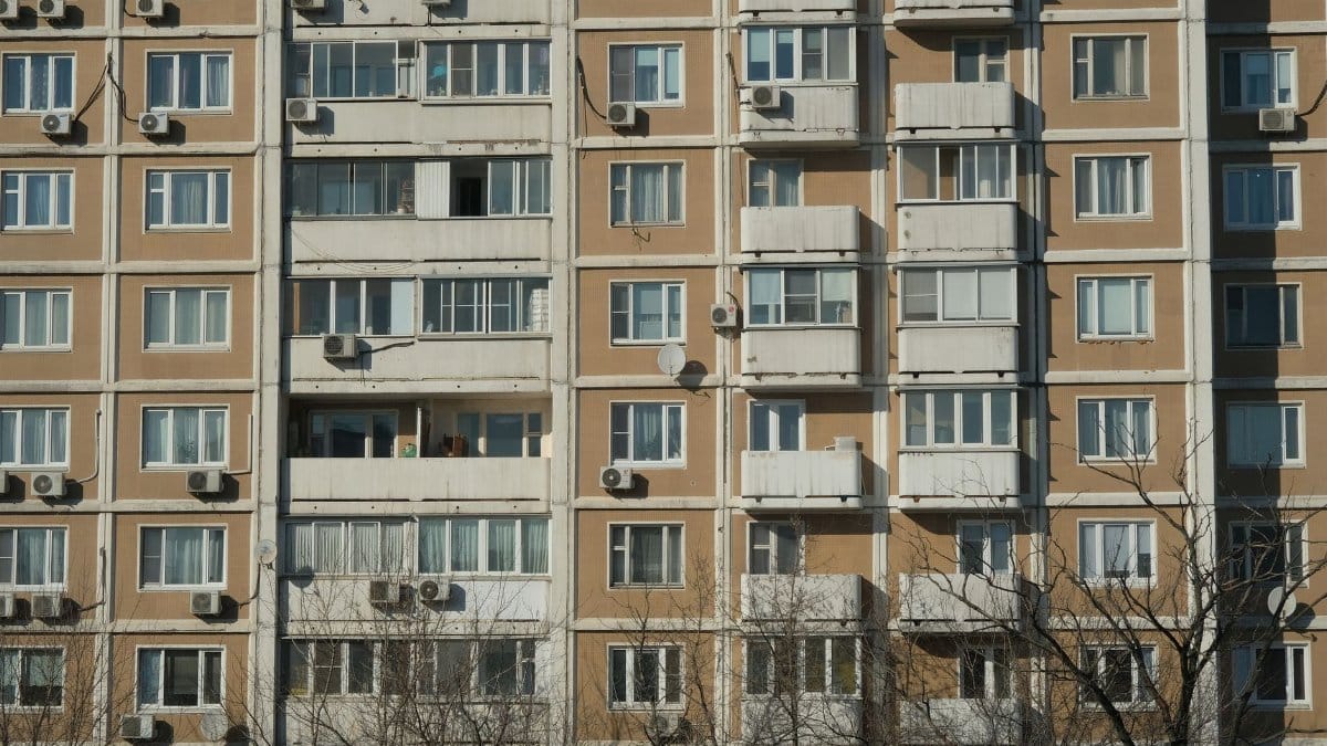 Front view of a sunlit urban apartment building with balconies and air conditioning units.