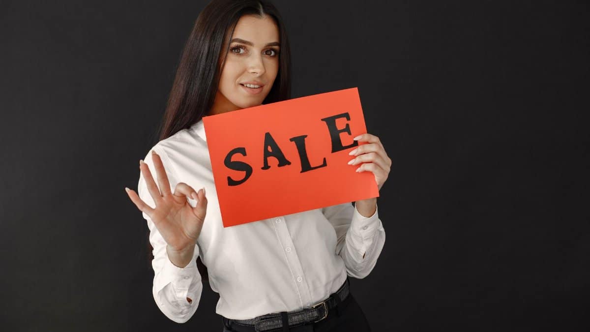Elegant woman in white shirt showing a red sale sign, ideal for promotional materials.