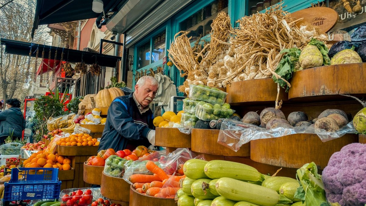 Bustling urban produce market with fresh vegetables and fruits, vendor attending to stall.