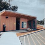 A wooden building at a roadside rest area with parking and a clear blue sky.