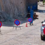A row of no parking signs on a cobblestone street with parked cars, emphasizing road restrictions.