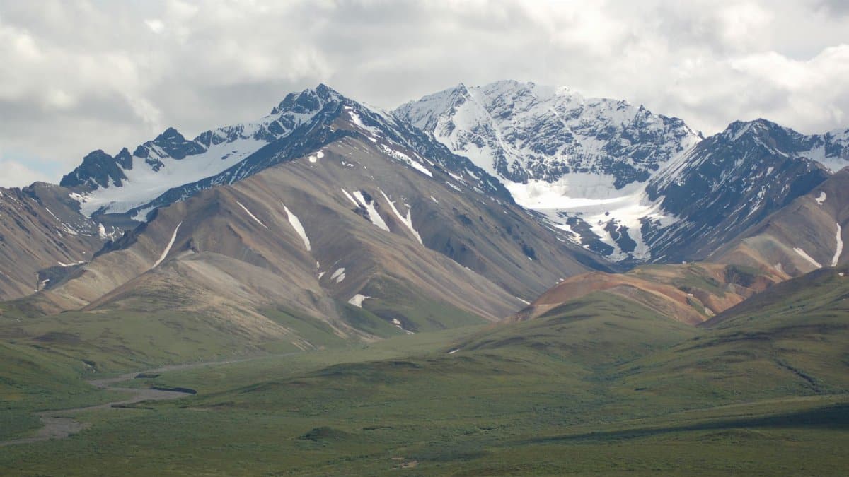 A breathtaking view of a snowcapped mountain range with lush green pastures under clouds.