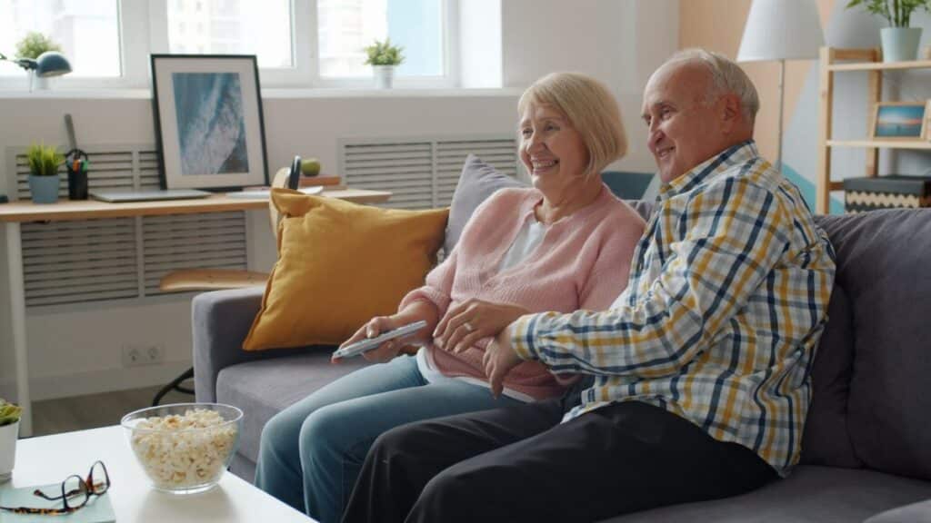 Elderly couple enjoying time together on the couch at home watching TV.