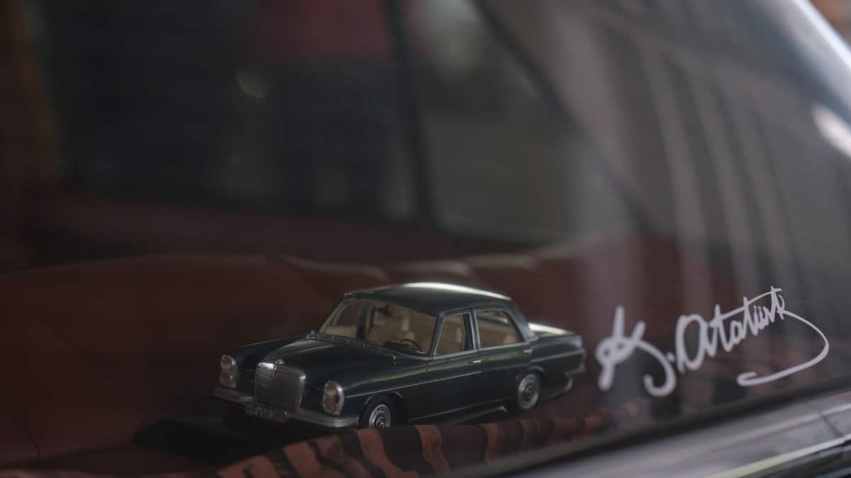 Close-up of a classic car model on display behind glass, featuring signature.