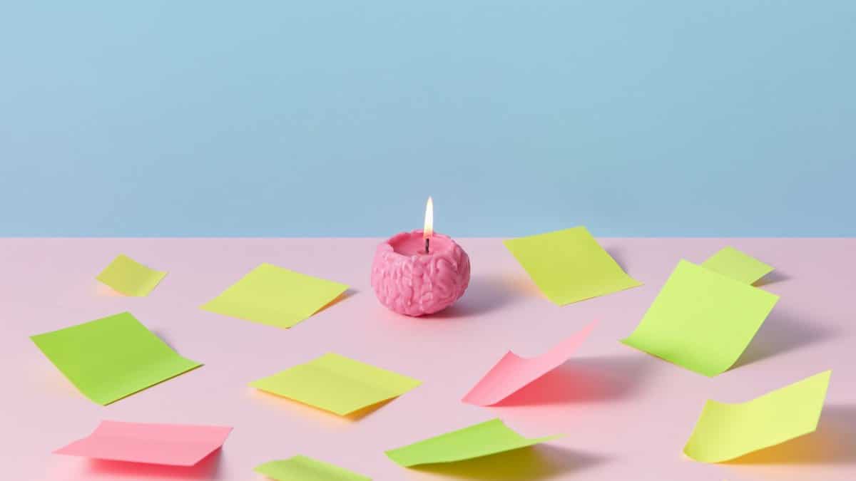 A pink brain candle lit among colorful sticky notes on pastel background, evoking creativity.