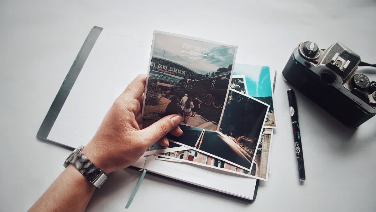 A person holding photos with a vintage camera and notebook on a desk.
