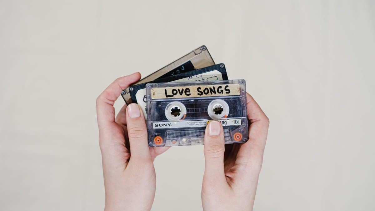 Hands holding cassette tapes labeled 'Love Songs', highlighting 90s nostalgia.