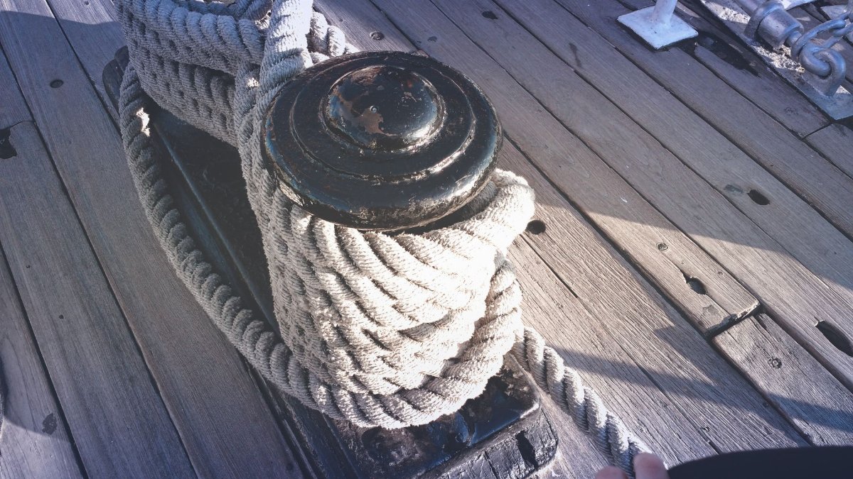Detailed view of thick nautical rope wrapped around a bollard on a wooden deck in daylight.