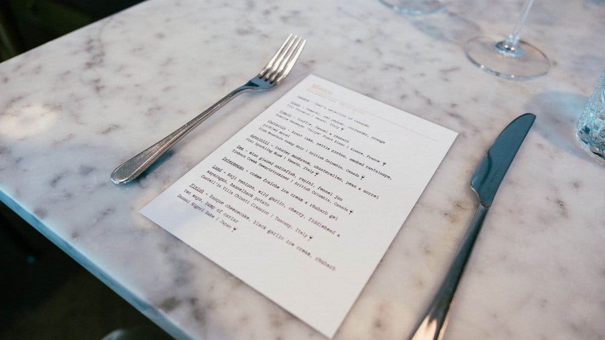 A marble table setting in an upscale restaurant featuring a menu, fork, and knife, offering a taste of fine dining.