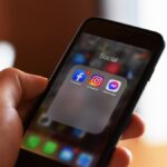 Close-up of hand holding smartphone showing social media apps like Facebook and Instagram.