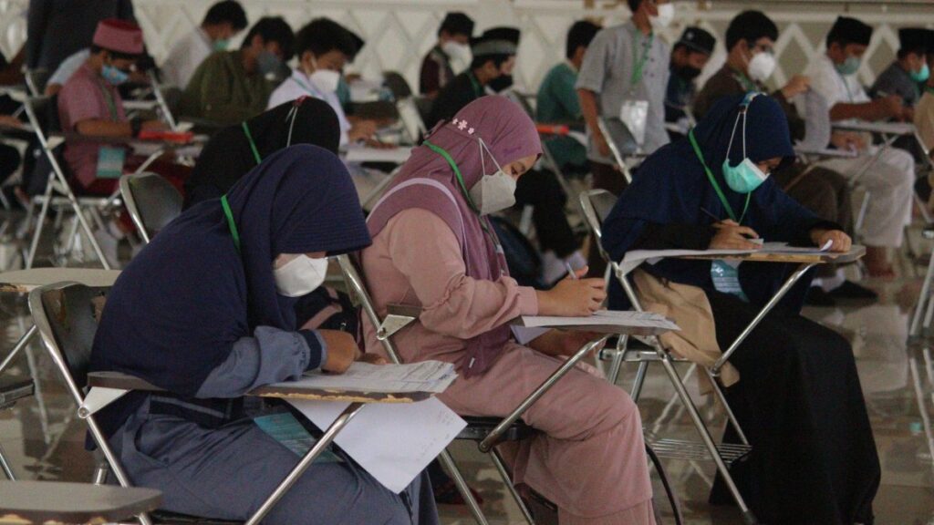 A diverse group of students wearing masks, concentrating on their exams in a classroom setting.