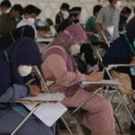 A diverse group of students wearing masks, concentrating on their exams in a classroom setting.