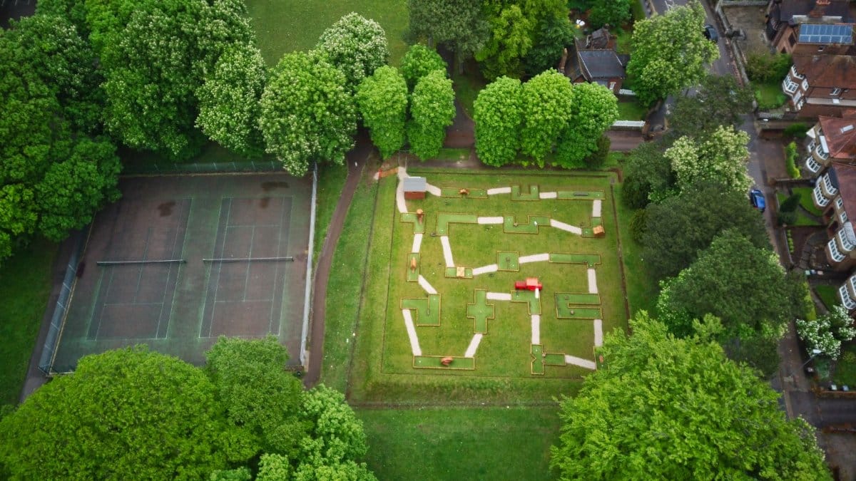 An aerial view of a miniature golf course and tennis court surrounded by lush greenery in Luton, England.