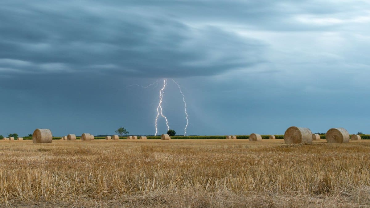 A striking image of lightning illuminating a rural hayfield under a stormy sky.